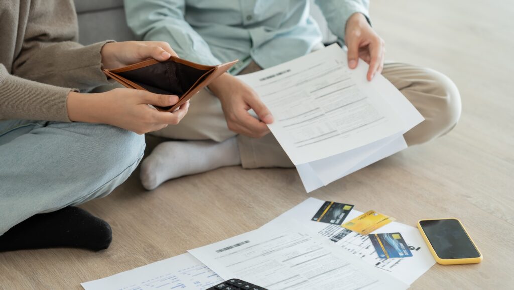 A couple sitting on the floor calculating their debt to represent ‘what do debt collectors do? ’