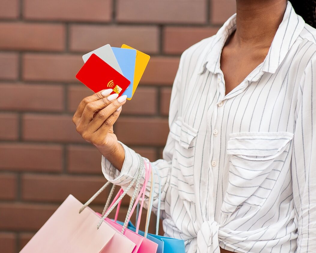 A woman carrying shopping bags on her arm and holding four store cards, demonstrating store card debt